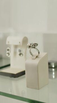 Vertical no people close-up of dainty set of platinum jewellery, earrings and ring inlaid with white pearl showcased in premium accessory showroom