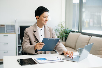 Young Asian man using laptop and tablet while sitting at her working place.