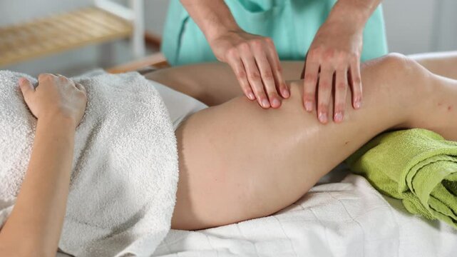Young male masseur massaging thighs of adult woman