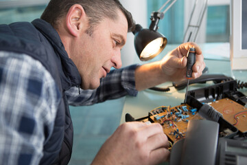 man working on an electronic circuit board with a screwriver