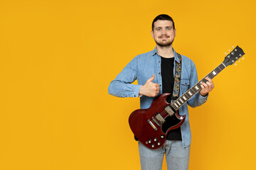 Attractive young guy with a guitar in his hands on a yellow background