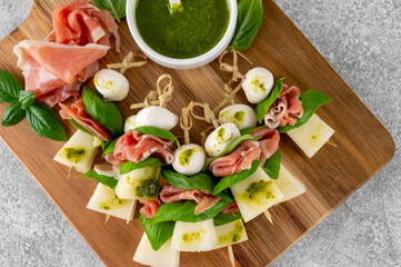 Appetizer with melon, mozzarella, prosciutto ham and fresh basil on stick with pesto sauce on a...
