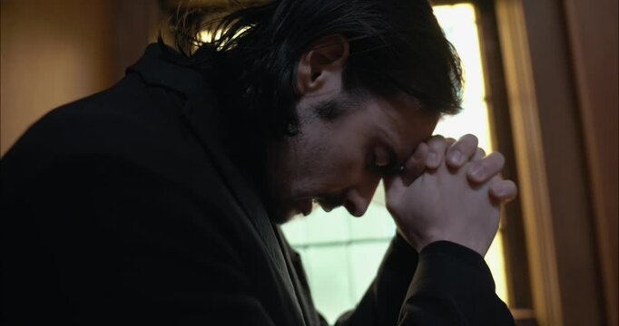 Young man in old church building in front of stained glass window kneeling, praying, worshipping. Christianity, worship, and prayer concept.