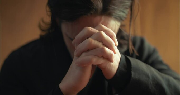 Young man in old church building in front of stained glass window kneeling, praying, worshipping. Christianity, worship, and prayer concept.