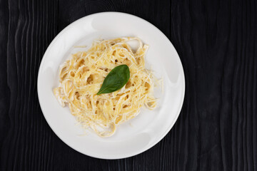 Pasta with sauce and basil in plate on black wooden background