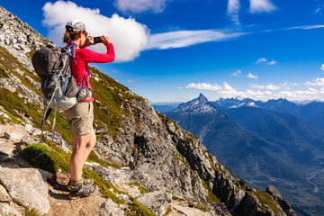Adventurous athletic female hiker taking a photo with her cellphone of jagged mountains in the in the Pacific Northwest.
