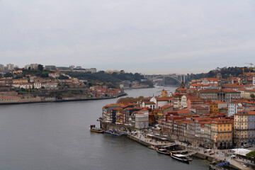 Scenic view of the Douro River with historical buildings and houses lining the waterfront in Porto, Portugal on a cloudy day.