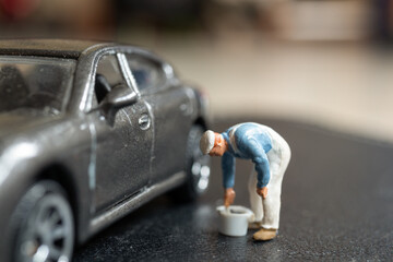Naklejka premium Miniature people, A worker bends over as if inspecting or repairing something on a sleek metallic gray car model blurred background keeps the focus on the miniature scene