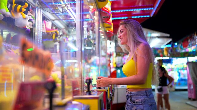 Happy caucasian blonde woman playing arcade games at fair at night