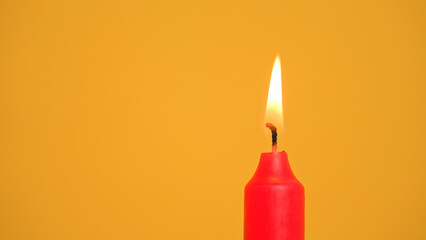 A red candle is burning brightly against a vibrant yellow background, creating a festive atmosphere suitable for Christmas, birthdays, or holidays.