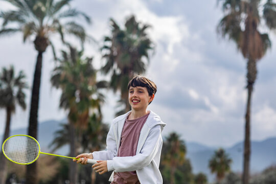 Boy playing badminton outdoors against palm trees background