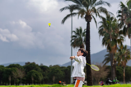 Boy playing badminton outdoors against palm trees background