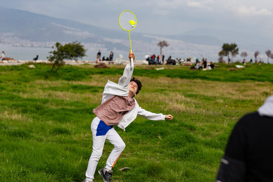 Boy playing badminton outdoors against sea and hills background