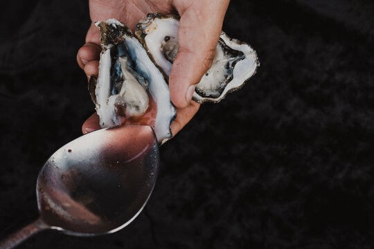 Hands holding fresh oysters with a spoon.