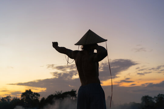 Man wearing an Asian conical hat in a rice field.