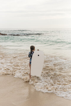 Young girl in rashguard waits with boogie board for the perfect wave.