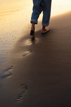 Man walks along the beach, bare feet on the sand.