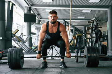 Lifts a barbell. Strong muscular man is working out in the gym
