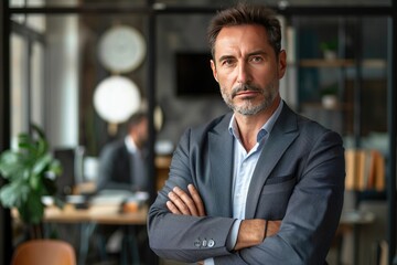 Fototapeta premium confident mature businessman standing with arms crossed and looking at camera in office