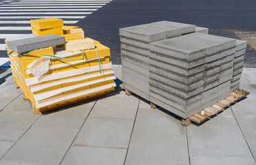 Street repair materials, stacks of yellow tactile paving and gray concrete tiles, placed on wooden...