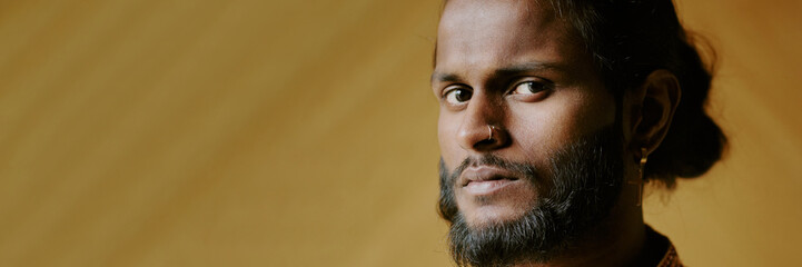 Website header shot of young Indian man with luxury nose ring and golden earring, his chocolate eyes looking in camera