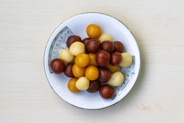 Delicious Bangladeshi sweets on a white plate on light wooden background. It is called Baby sweet because little in size. Very juicy and tasty sweet.