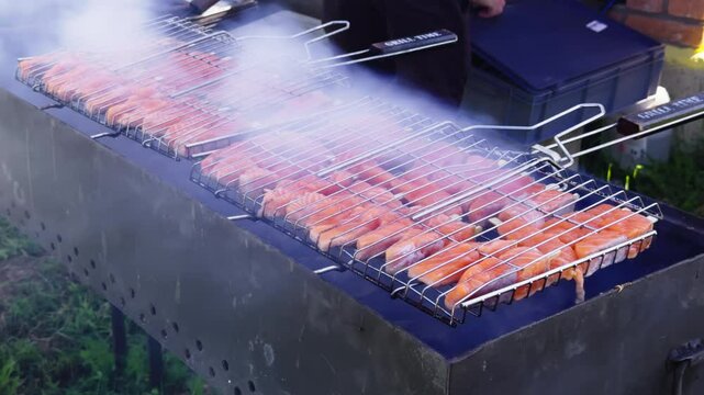 Picnic with friends. Summer barbecue with friends. Grilled fish. Salmon redfish on the grill cooks slowly and smoke comes out. Outdoor grill. Food and Catering. Grilled red salmon skewers