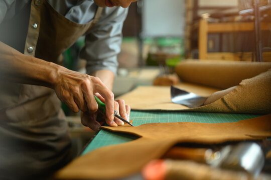 Cropped shot of artisan working on the workbench with different rolls brown leather