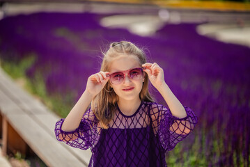 A young girl in a purple dress and sunglasses enjoys the warm sunlight in a field with purple sage