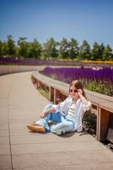 A young girl is basking in the warm rays of the sun, enjoying the beauty of the park, overgrown with bright purple sage. Her white shirt and blue trousers complete the landscape