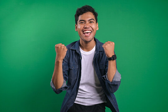 Portrait of satisfied young Asian man celebrating success over green background