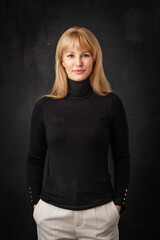 Studio portrait of a blond haired woman standing against isolated dark background