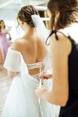 Naklejka premium Bridesmaid is helping the bride to dress. Morning of wedding day