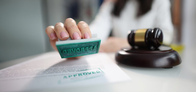 Close-up of female hand holding approved stamp, judge gavel. Judicial system, justice and low. Judge, trial, litigation and court decision concept