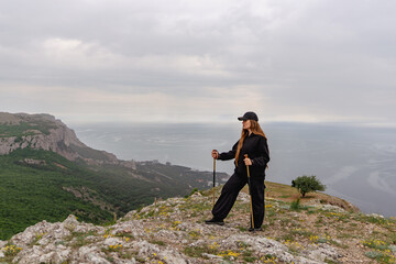 Obraz premium A woman stands on a mountain top with her arms crossed and a hat on