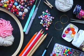 Colorful beads, coloring pencils, glitter, needles, string, hoop, tape and scissors on dark...