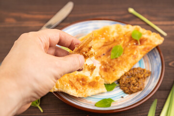 Fried homemade khachapuri cake with cheese and meat, fried in pan with hand on brown wooden. Side view, close up, selective focus