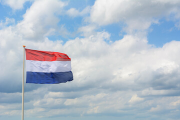 Dutch flag in the wind with a cloudy sky as background. One Dutch flag on the summer day