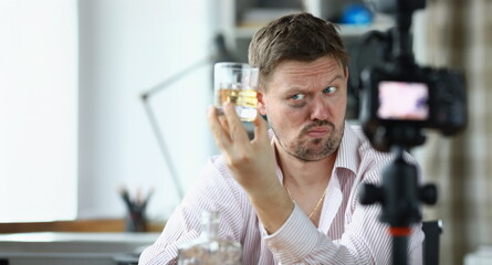 Portrait of video blogger making content for internet channel. Man showing glasses with alcohol drink and looking incredulously. Blogging and vloggonig concept