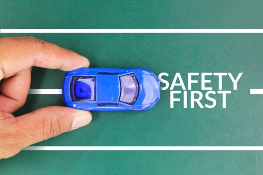 hand holding the car with the words SAFETY FIRST, to remind the driver to drive carefully and avoid distraction while on the road. safe driving concept - Powered by Adobe