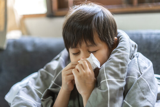 Young asian boy sneezing or blowing his nose and mouth with tissue, cold allergies or illness, health, virus and flu season, RSV, Influenza, childcare and hygiene practices, especially for children
