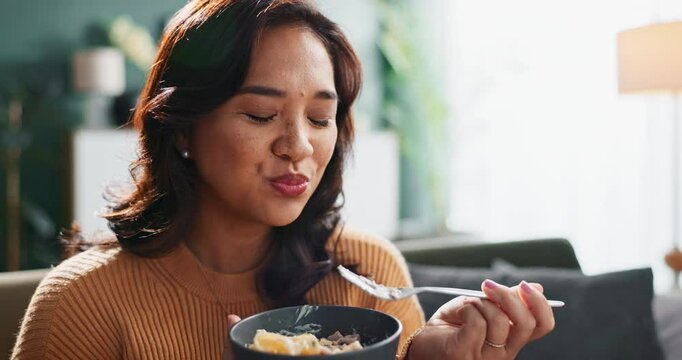 Asian, woman and eating dinner in home with enjoyment for healthy meal, nutrition and reward on sofa. Person, pasta and food on couch in living room for lunch, hungry and happy with flavor in house