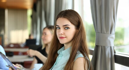 Portrait of cute young woman at business meeting in office. Smiling manager holding clipboard and looking at camera. Management and business concept