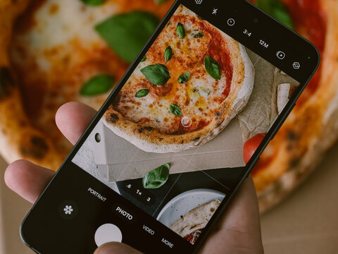 A man takes a photo of a pizza with his smartphone