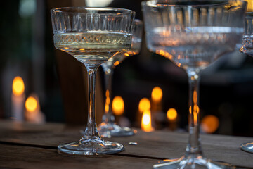 Shiny glass transparent glasses on a tall stem with a transparent drink, in the dark against the background of candle lights