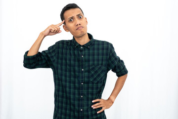 An Asian man wearing a casual green checkered shirt gave off an angry expression while pointing his finger at his brain to tell it to think. Isolated white background.