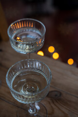 Shiny glass transparent glasses on a tall stem with a transparent drink, in the dark against the background of candle lights
