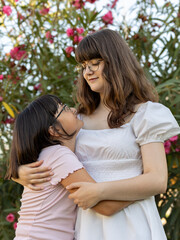 Fototapeta premium Teenage girl hugging younger sister in a garden, looking at each other with admiration