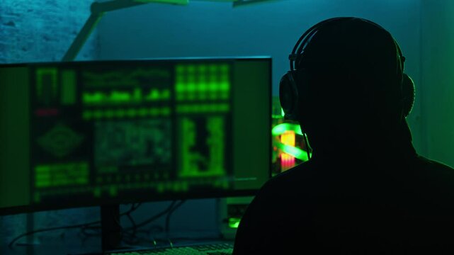 Hacker is sitting alone, engaging in wiretapping and spying on people using a computer. Medium shot. Slow motion.