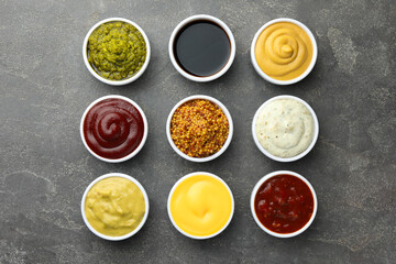 Many different sauces in bowls on grey table, top view
